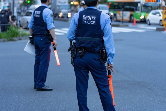 交差点で交通整理を行う警視庁の警察官。青い制服とベストを着用し、誘導灯を持っている。