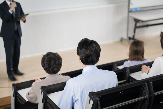 セミナー会場で、前方の講師の話を聞いている複数の参加者の後ろ姿