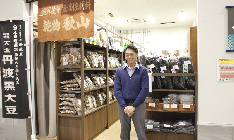 店舗前に立つ清光商事株式会社 乾物秋山 代表取締役 秋山 竜吾氏の写真