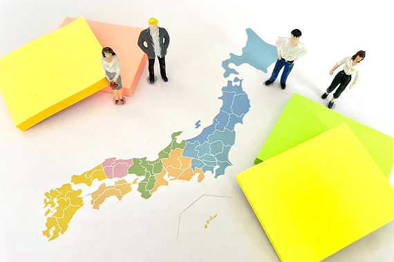 色分けされた日本地図の上に、イエロー・グリーン・オレンジの付箋と４体のビジネスパーソンのミニチュアフィギュアが配置され、地域をまたいだ脱炭素経営の普及・連携をイメージさせるビジュアル